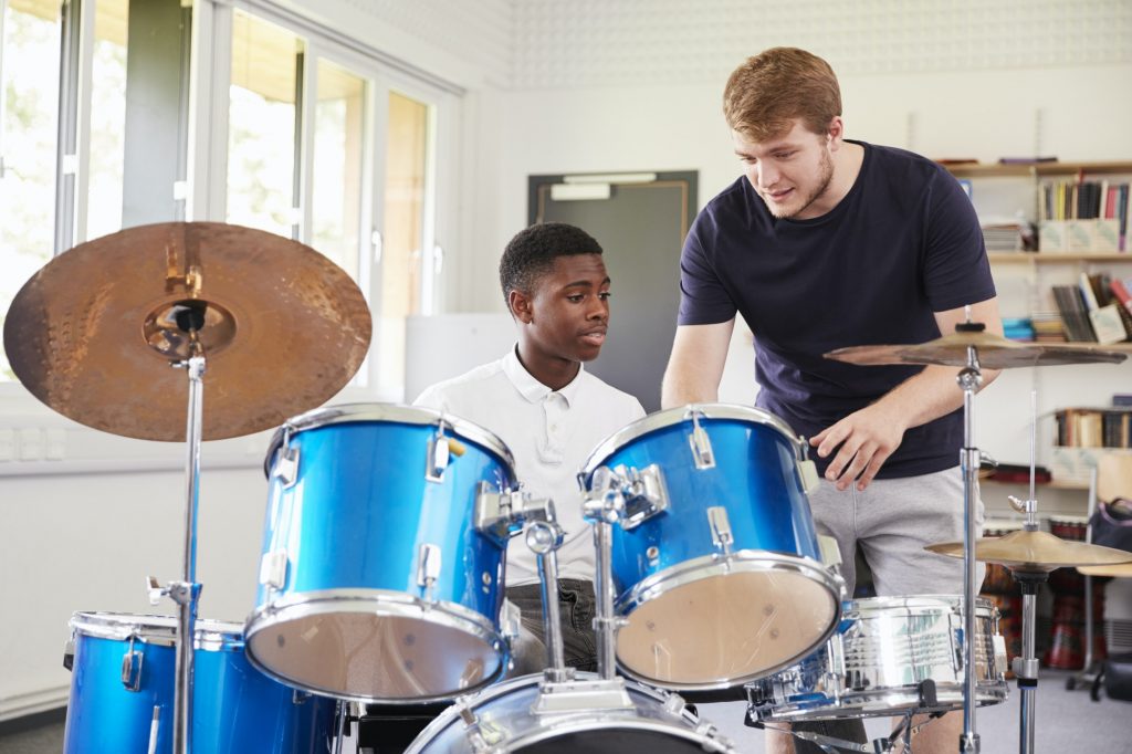 male-pupil-with-teacher-playing-drums-in-music-lesson